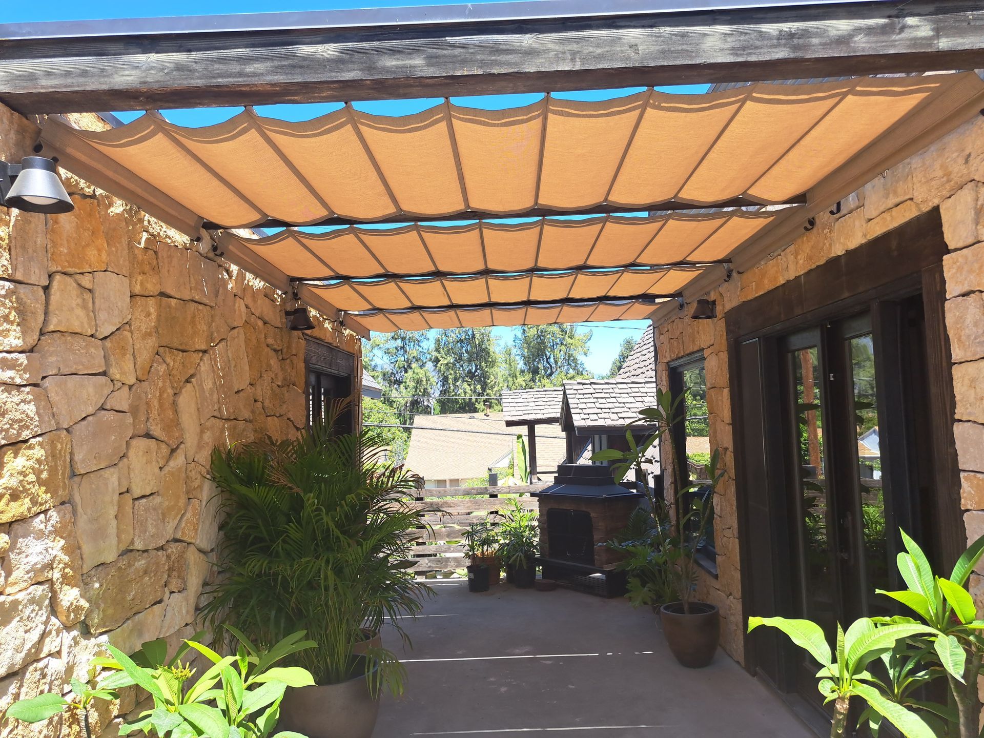 Stone patio walkway with a wood pergola, potted plants, and glass doors beside a stone wall