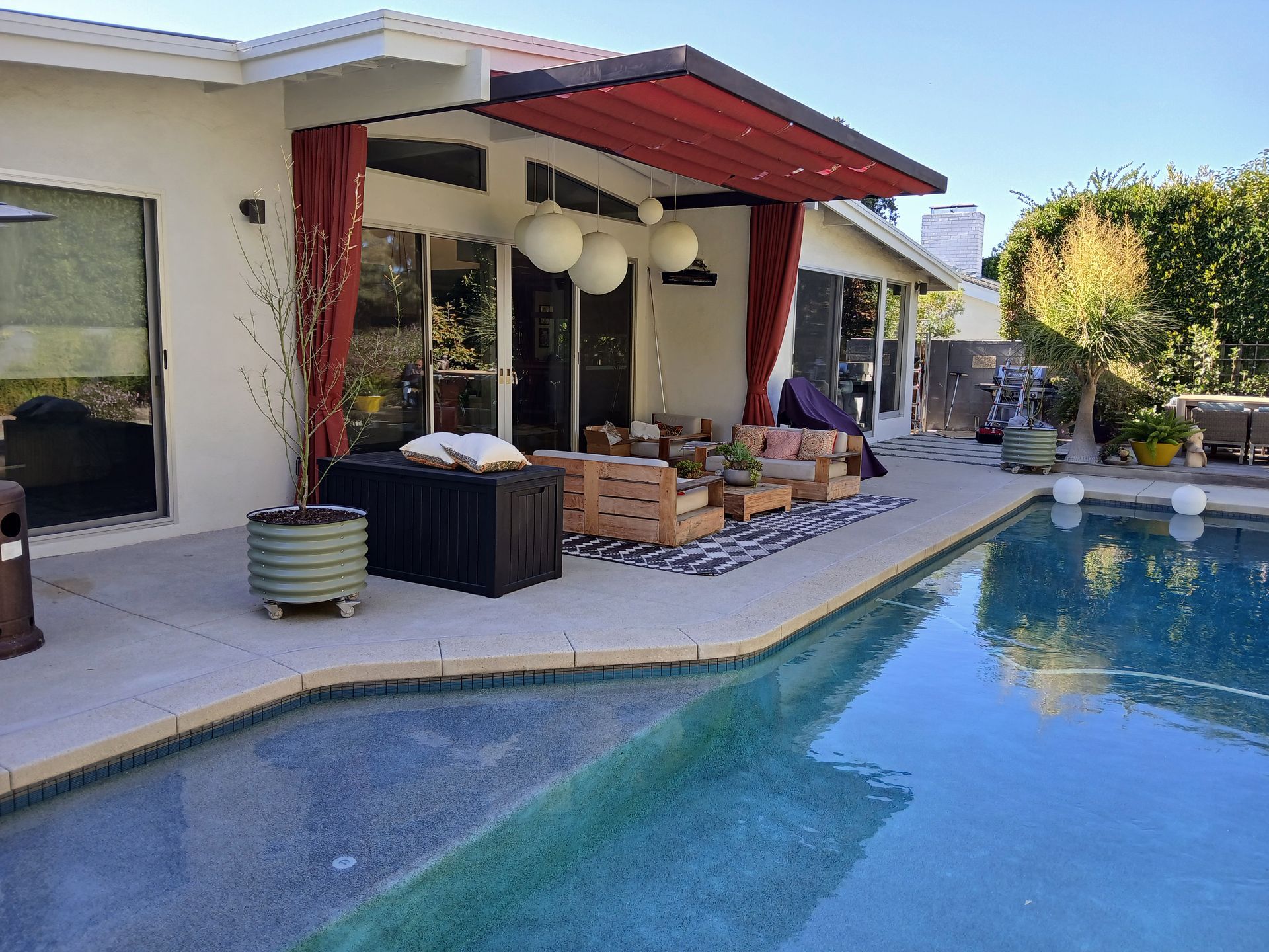 Modern patio beside a pool with lounge seating, pergola, and slide on wire awning panels