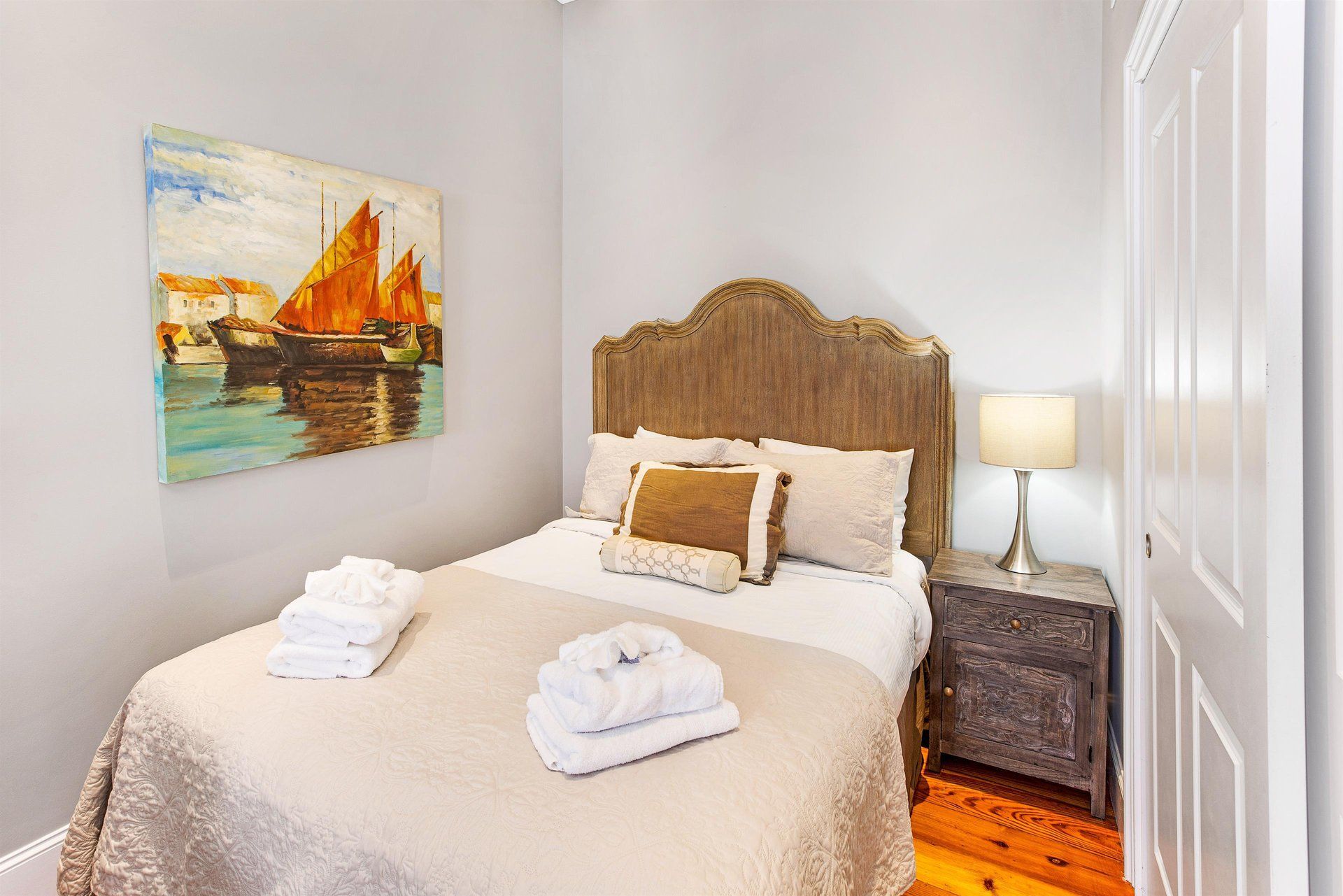 Bedroom with bed, art, nightstand, and towels. Neutral colors, natural light.