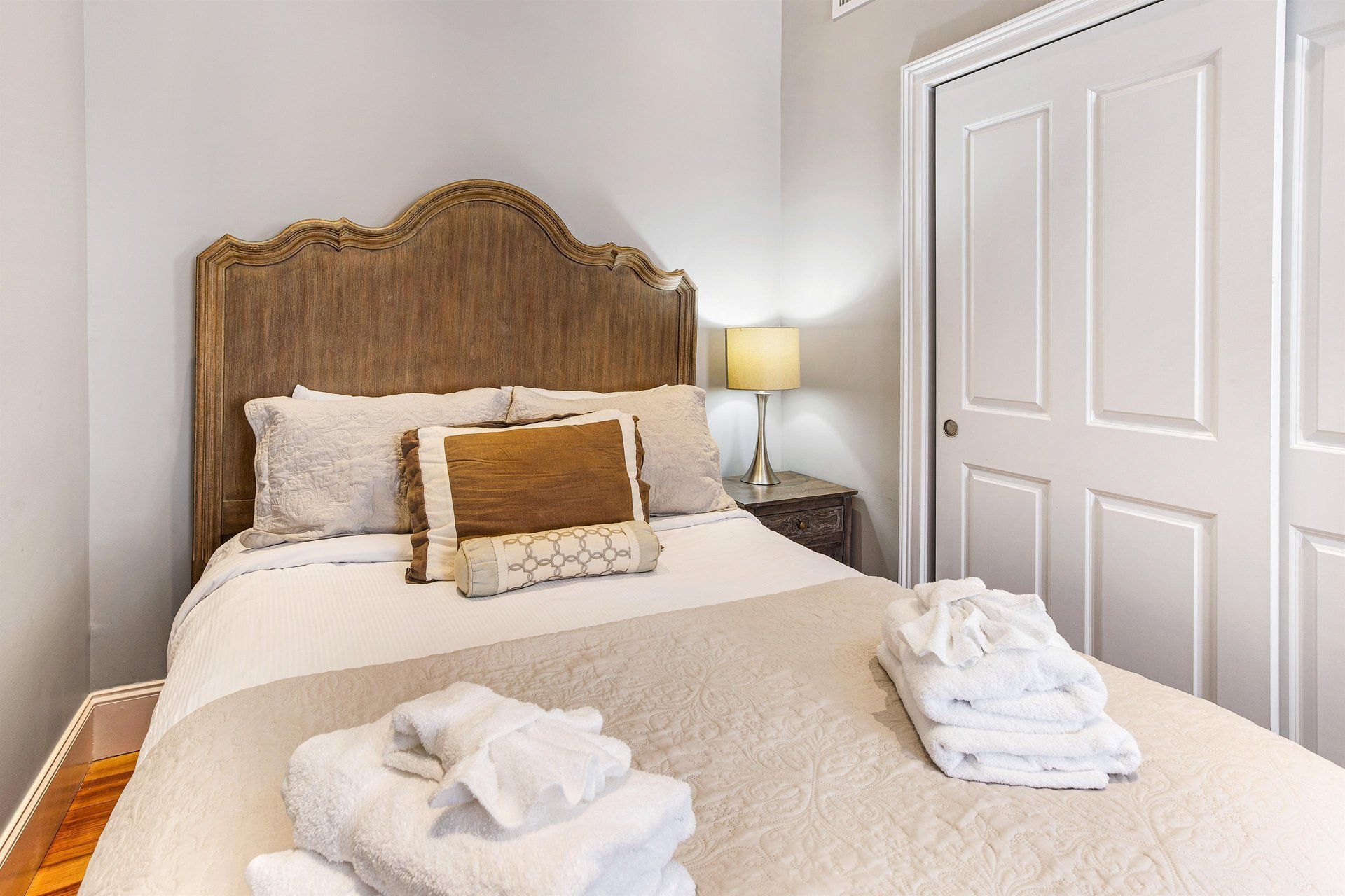 Bedroom with a bed, headboard, nightstand, lamp, and closet. Beige and white tones dominate.
