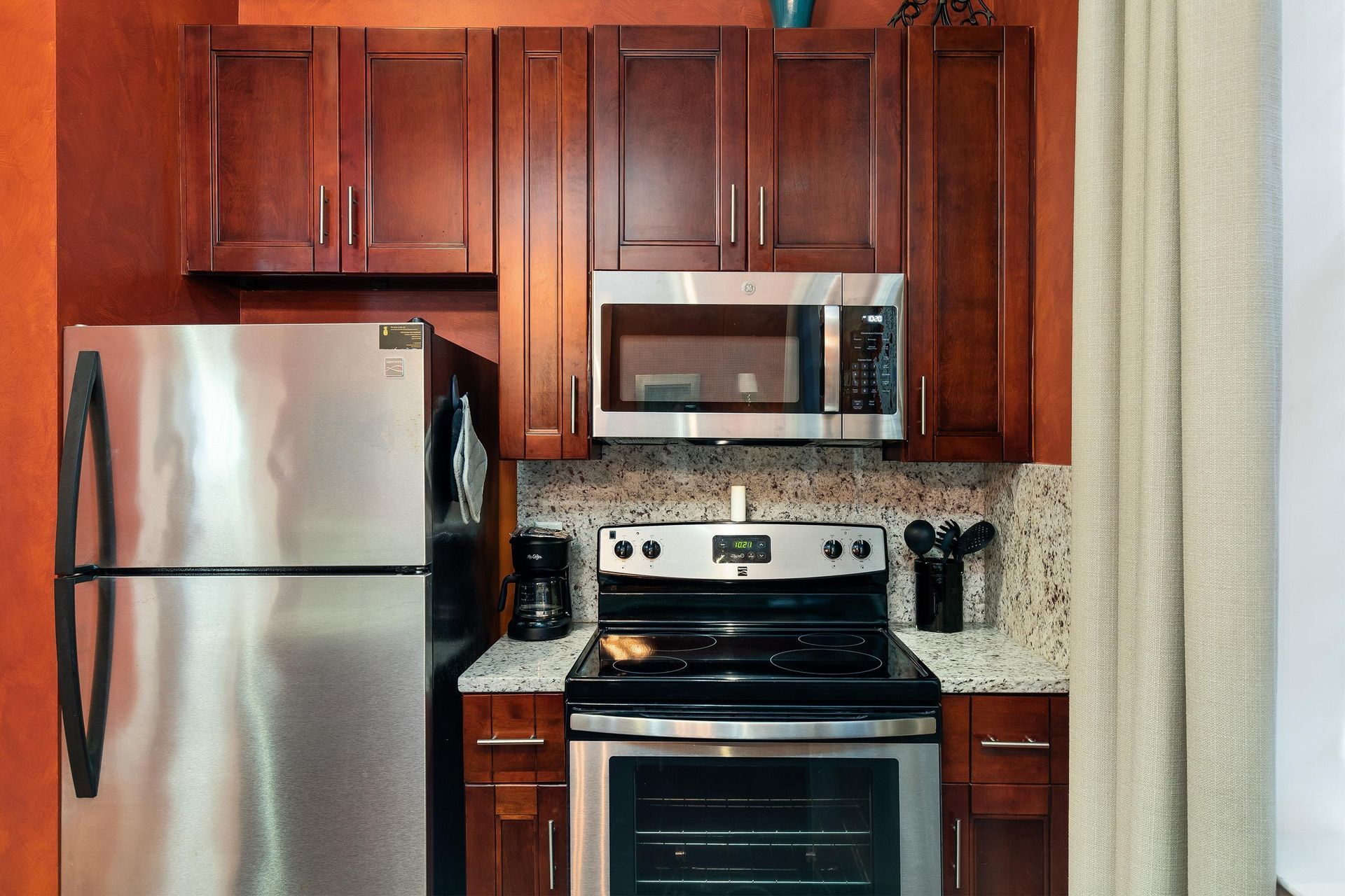 Stainless steel refrigerator, range and microwave with a granite backsplash.