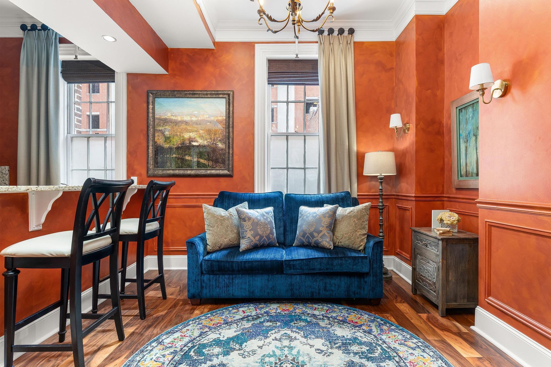 Cozy sitting area with a blue loveseat, bar stools, wall sconces and warm terracotta walls.