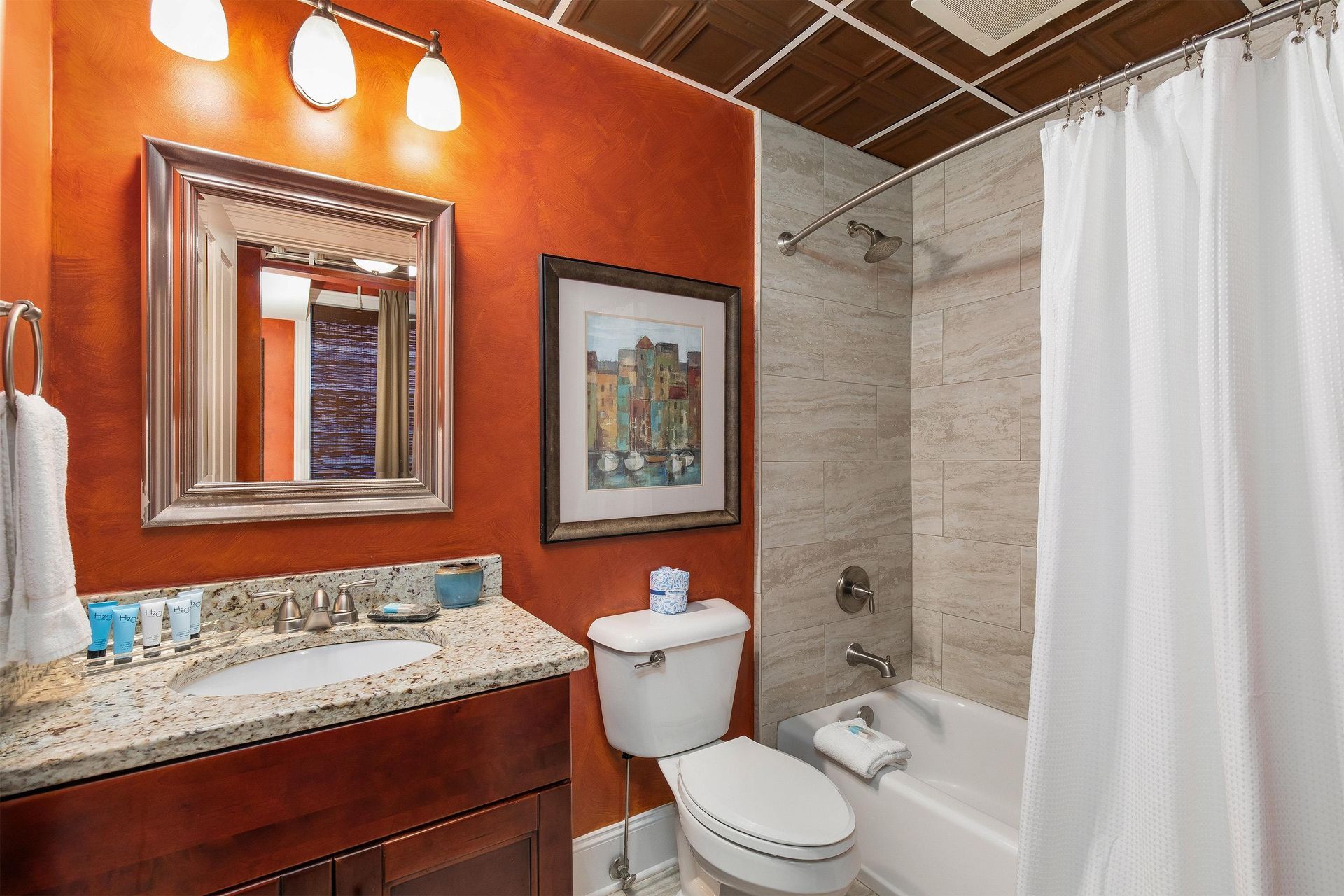 Bathroom with a granite vanity, framed mirror and tub-shower with a white curtain.