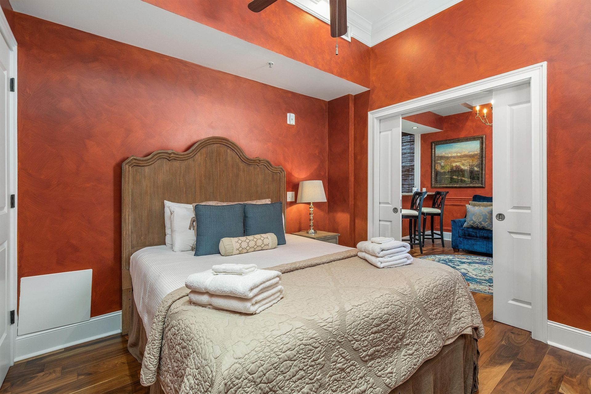 Bedroom with a carved wood headboard, fresh towels and a doorway to the living area.