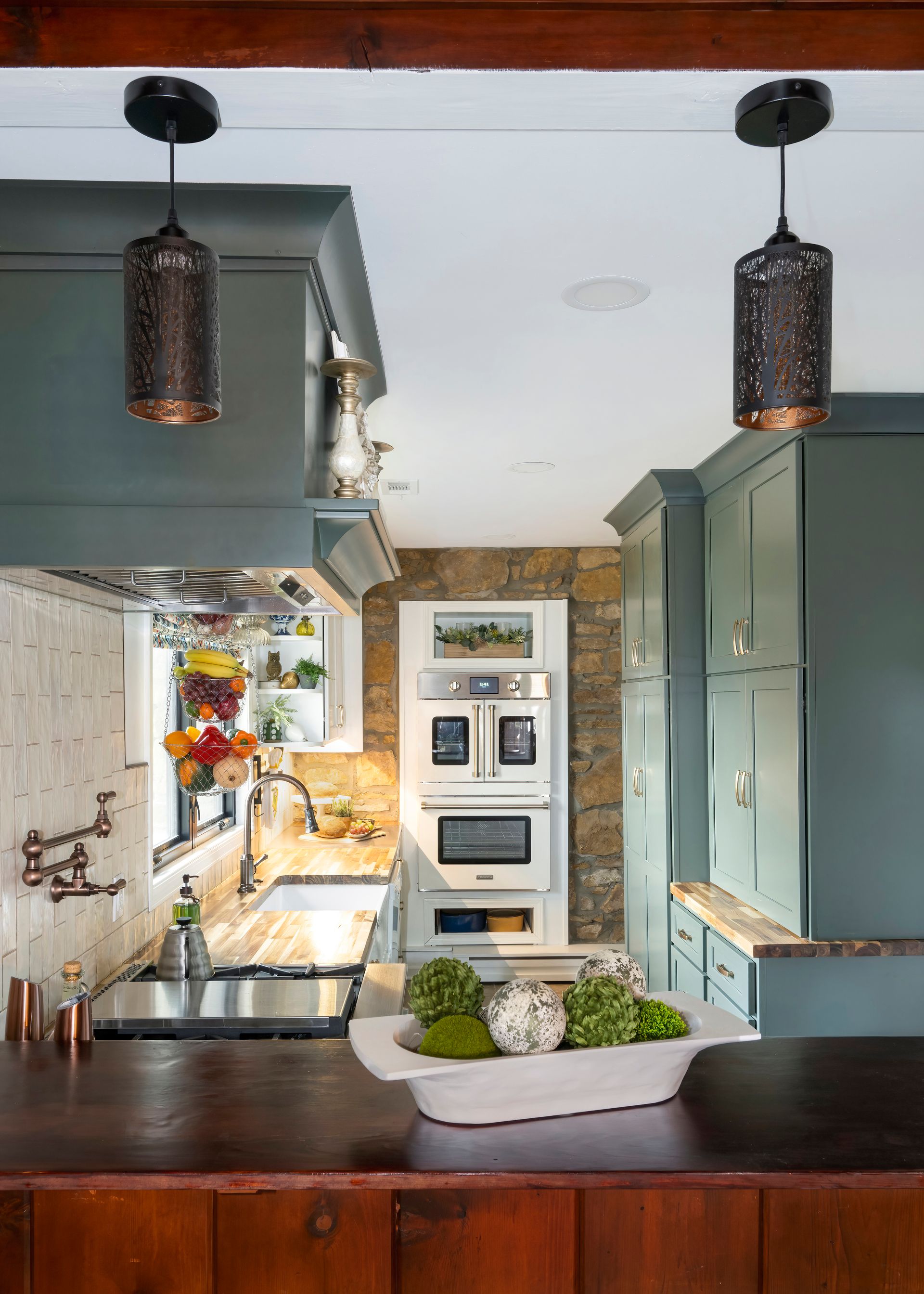 Kitchen with teal cabinets, stone wall, and rustic pendant lights.