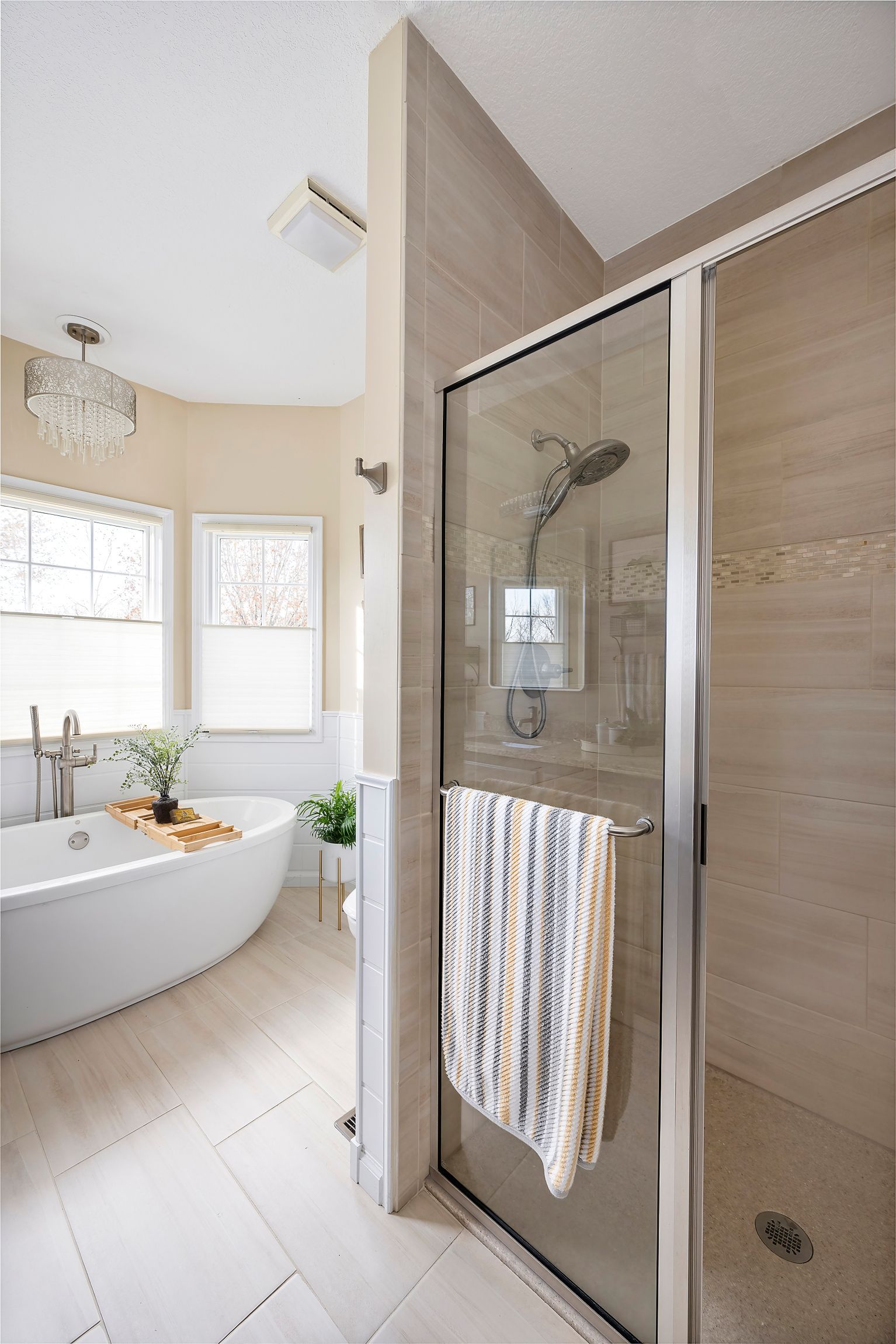 Bathroom with a freestanding tub, glass shower, and neutral-colored tiles.