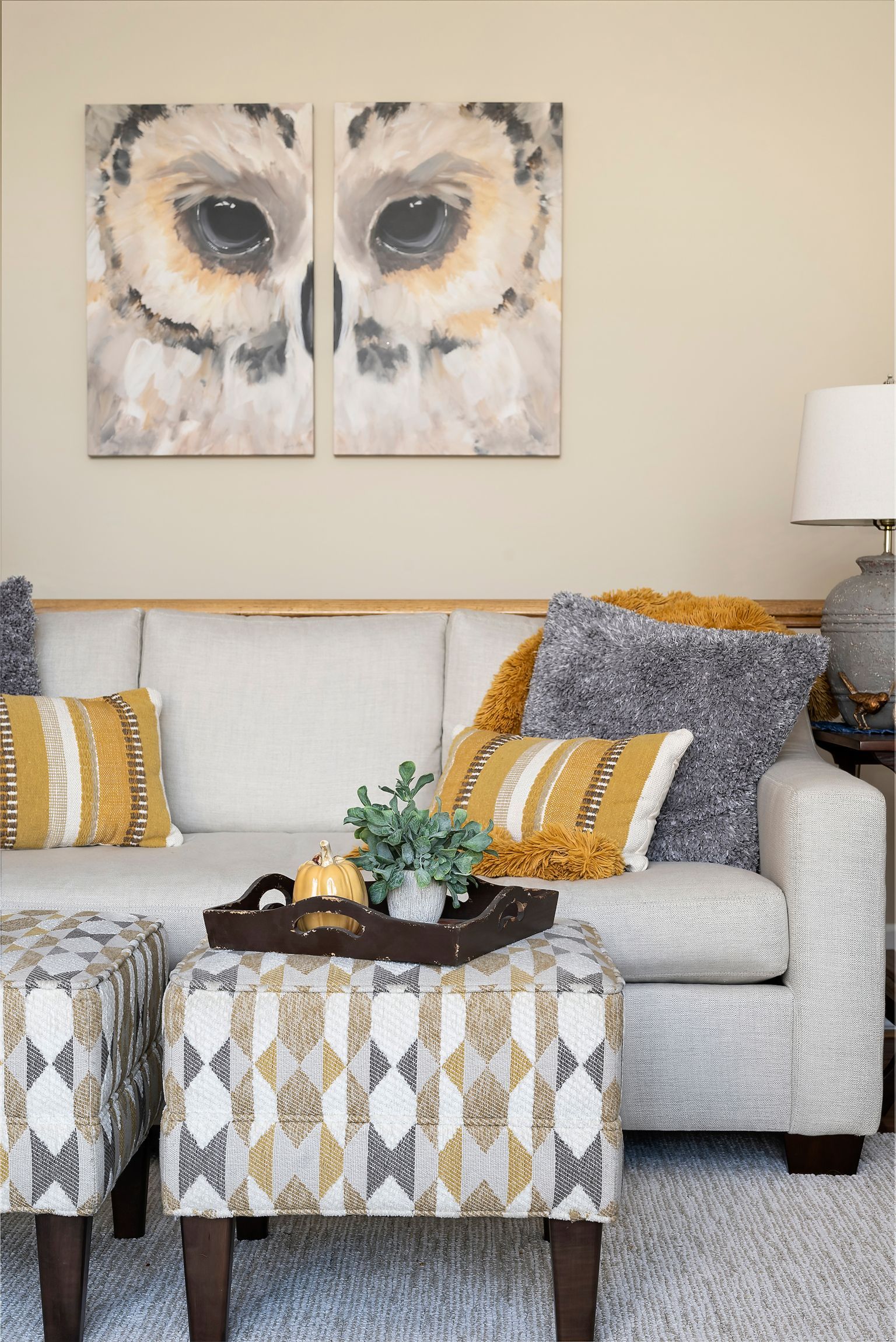 A living room with a couch , ottoman , coffee table and two paintings on the wall.
