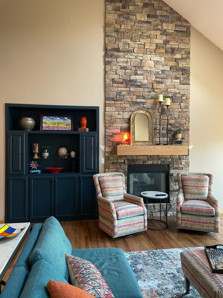 Living room with stone fireplace, built-in shelving, two patterned armchairs, and teal sofa.