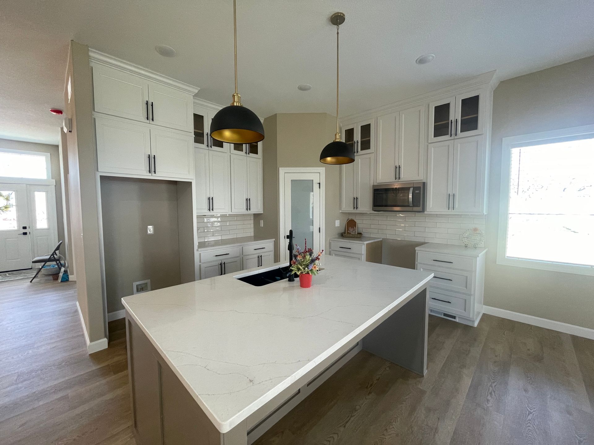 Kitchen with white cabinets, large island, pendant lights, and light-colored flooring.