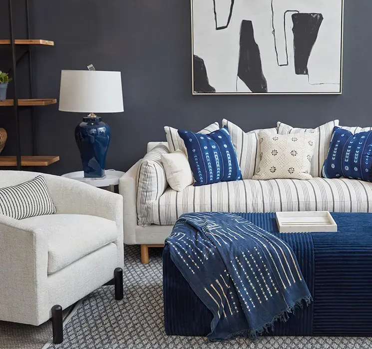 Living room with navy blue and white décor. Sofa, armchair, ottoman, lamp, and art.