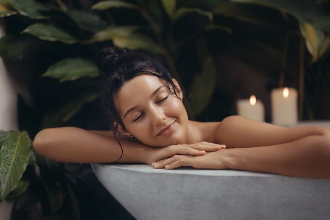 Woman with closed eyes, sunlight, hand in hair, palm leaves, and sun-kissed skin.