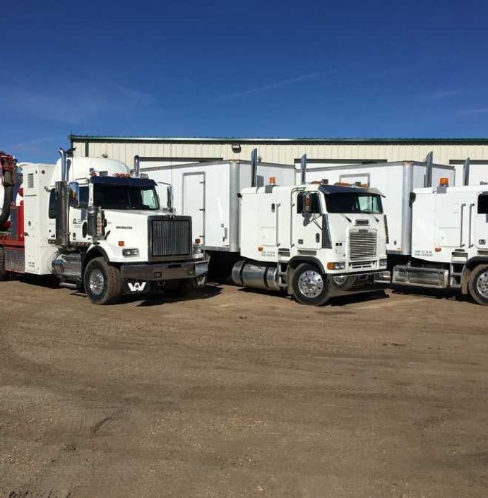 A row of white semi trucks parked in a dirt lot