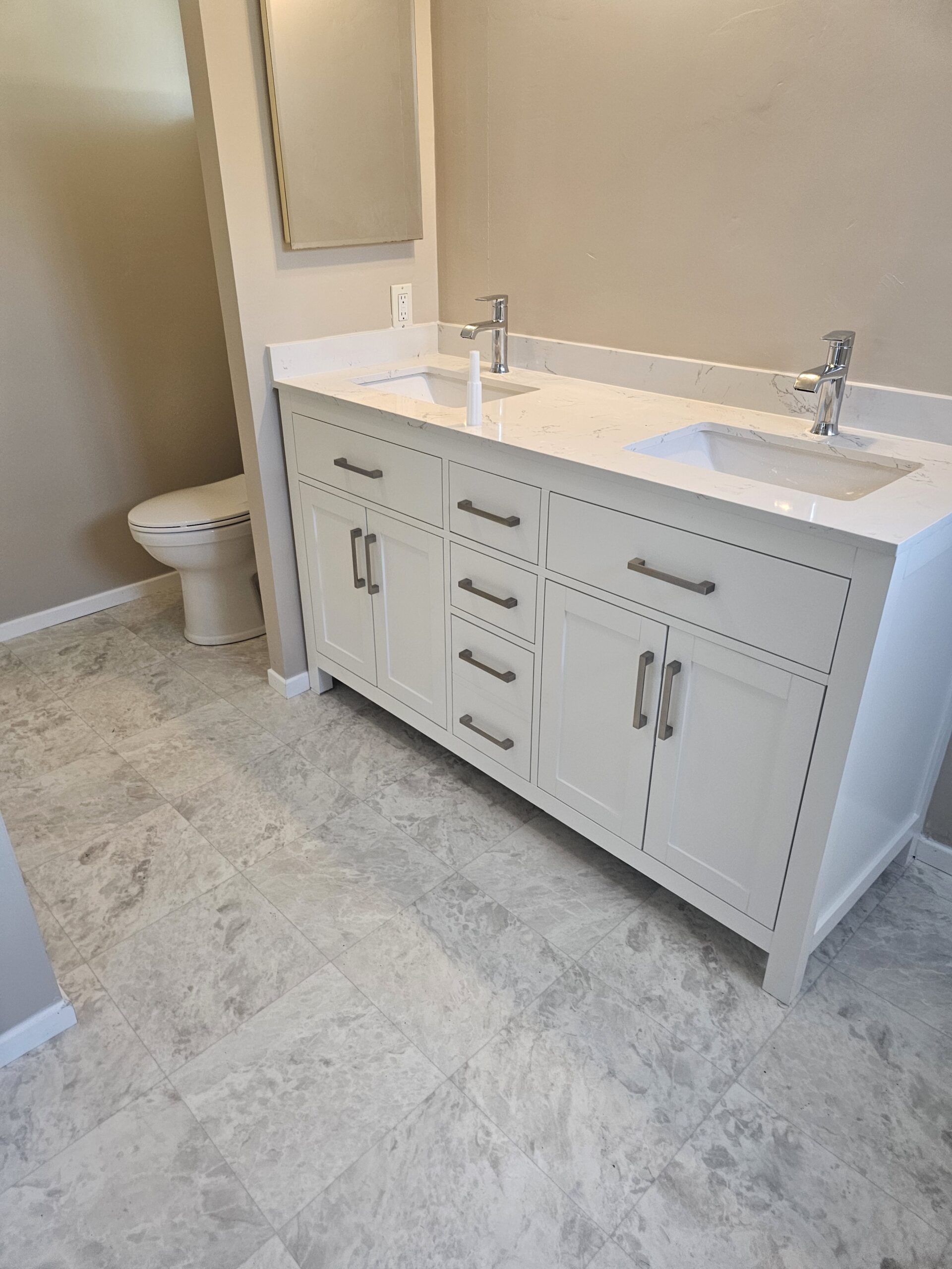 A modern bathroom featuring a white double vanity cabinet with chrome fixtures, a marble-patterned floor, and a toilet.