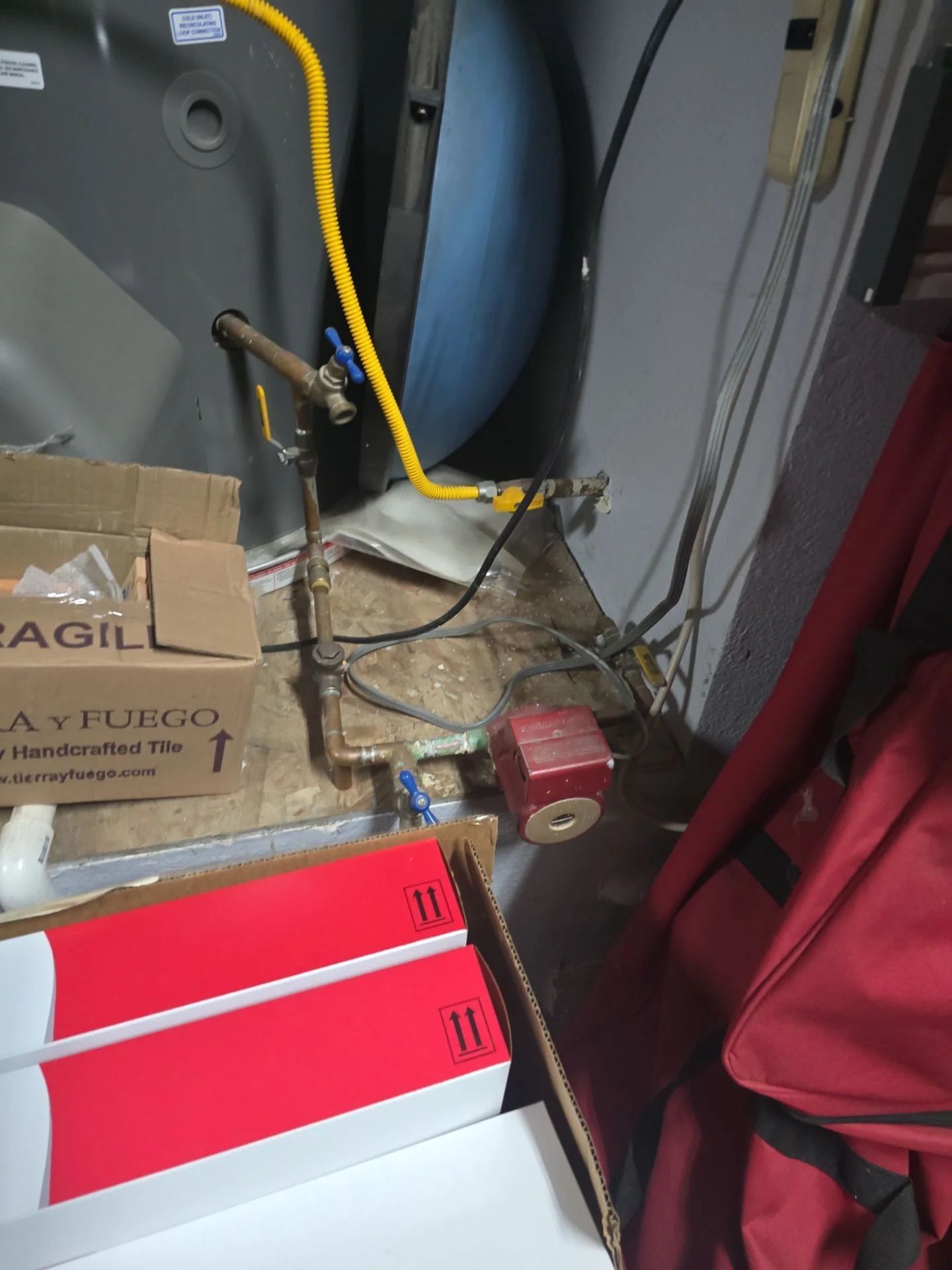 A close-up view of water pipes and a red circulation pump connected to a water heater in a cluttered utility space.