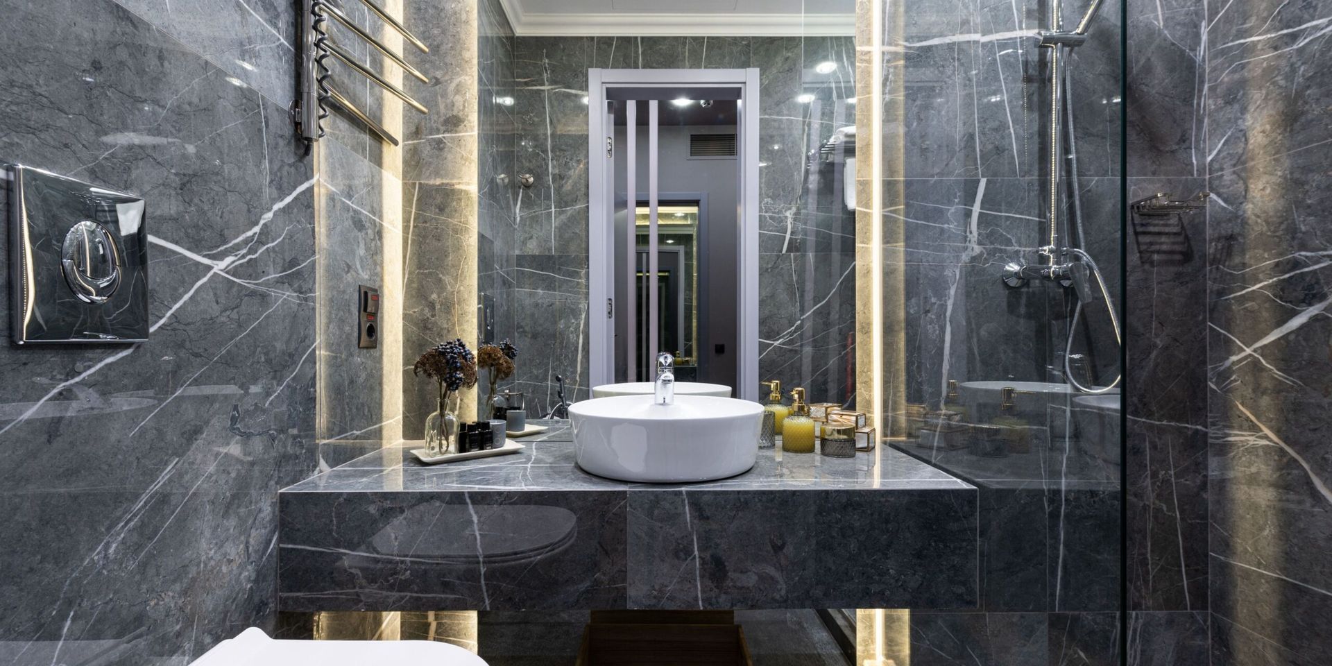 A modern bathroom with grey marble walls, a white vessel sink on a floating stone vanity, and warm recessed lighting.