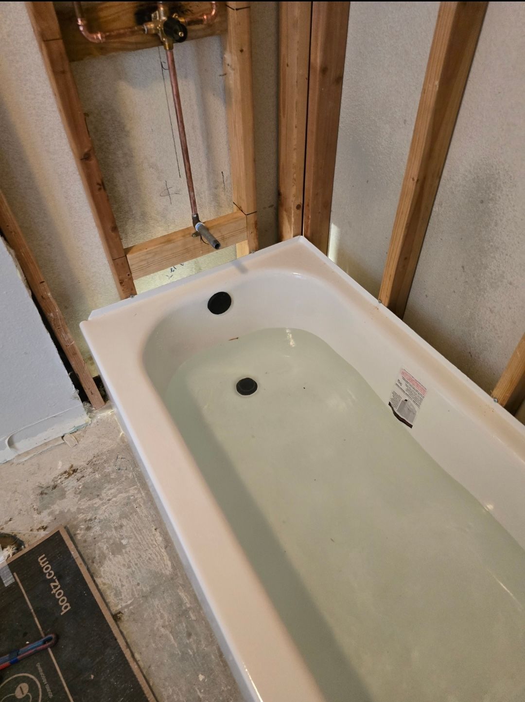 A new white bathtub sits in an unfinished bathroom frame with exposed wood studs and visible plumbing.