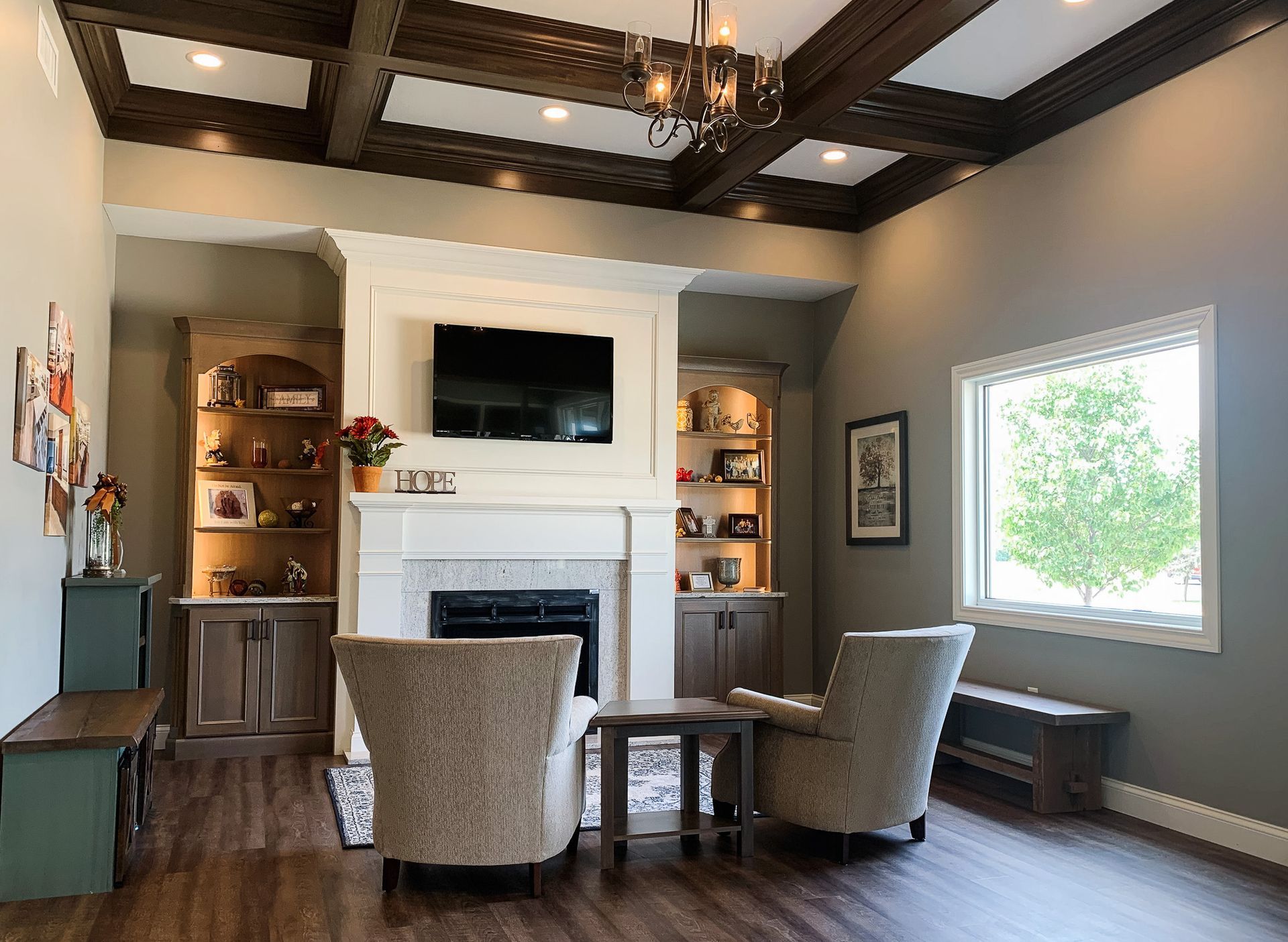 A showroom with wooden floors, a fireplace, and flatscreen tv on the wall with two chairs and a coffee table.