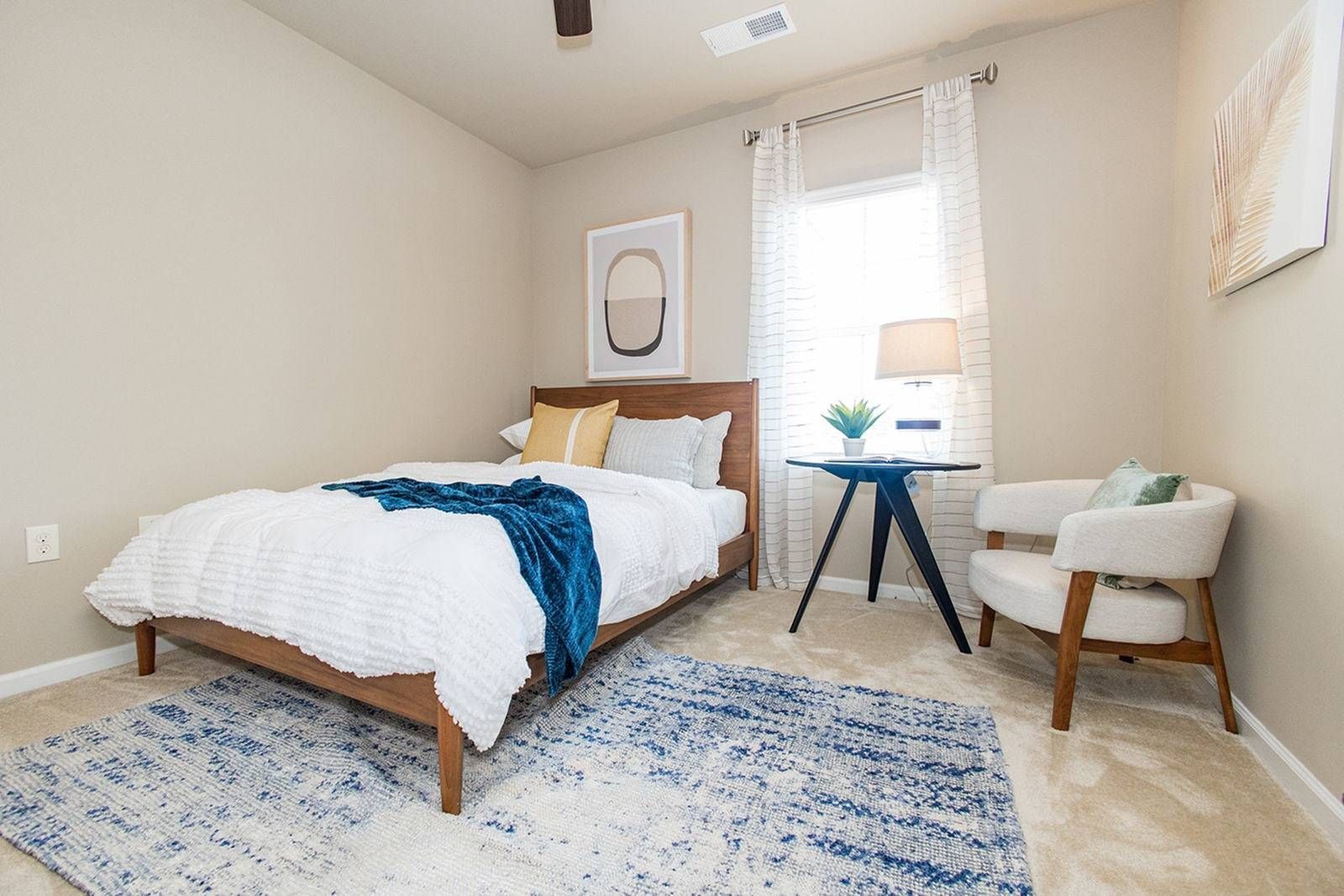 Bright bedroom with white bed, teal rug, bedside lamps, and window with sheer curtains