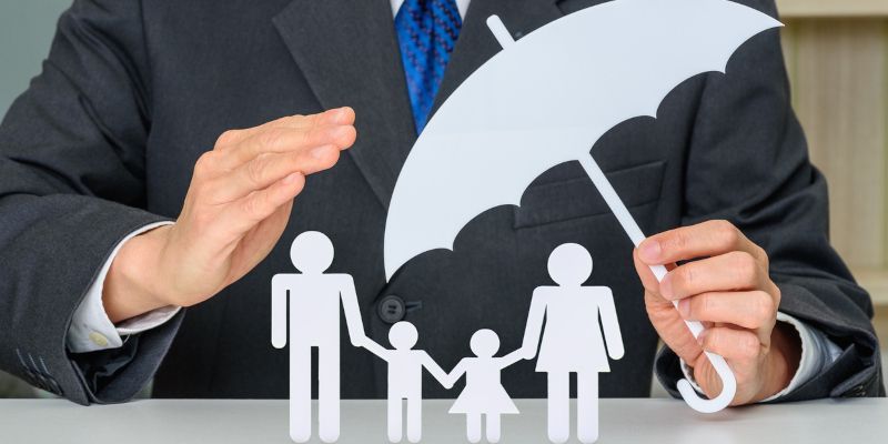 A person in a suit protects a paper family with an umbrella, symbolizing insurance.