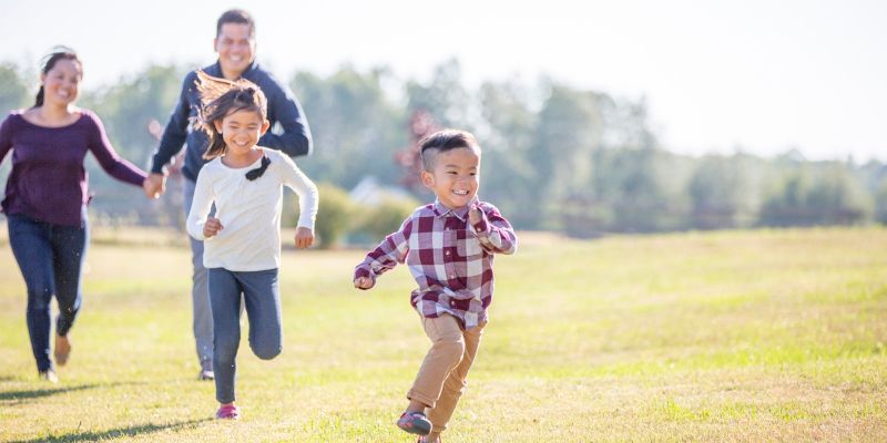 Family of four runs through a grassy field on a sunny day.