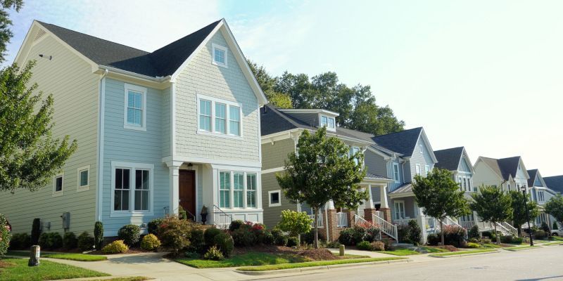 Row of colorful houses with green lawns and trees on a sunny day.