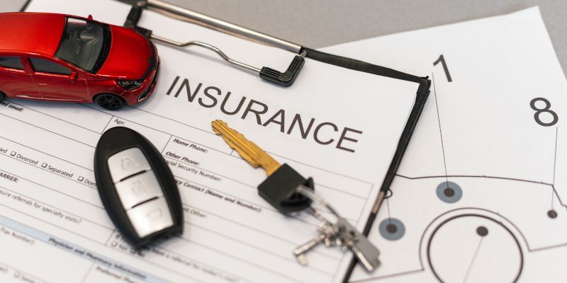 Red toy car, car keys, and key fob on an insurance document, top view.