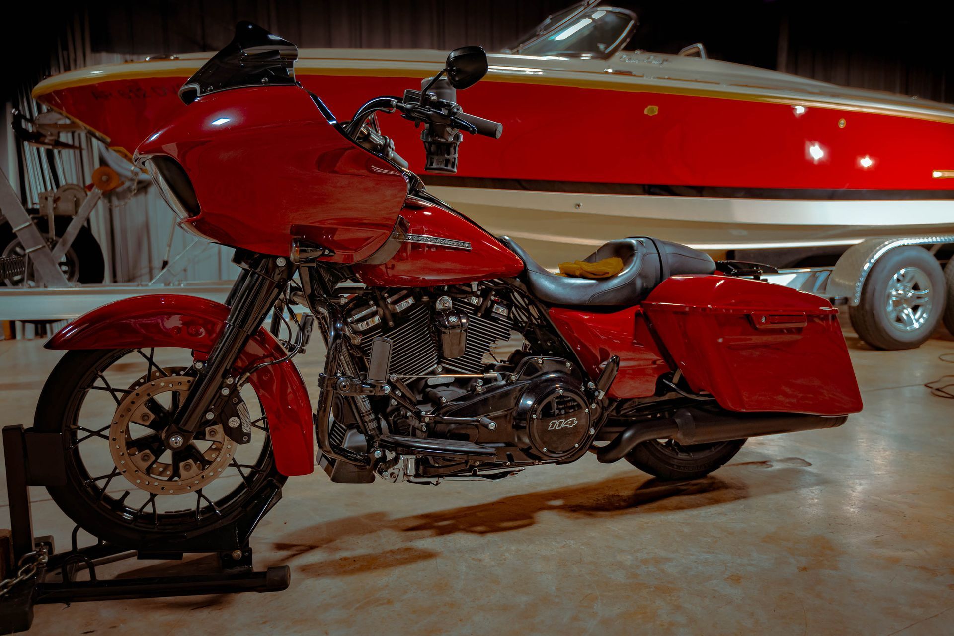 Red motorcycle parked in front of a red and white boat on a trailer.