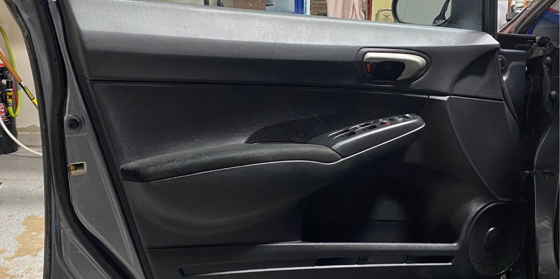 A black car door interior, showing the armrest, handle, and power window controls.