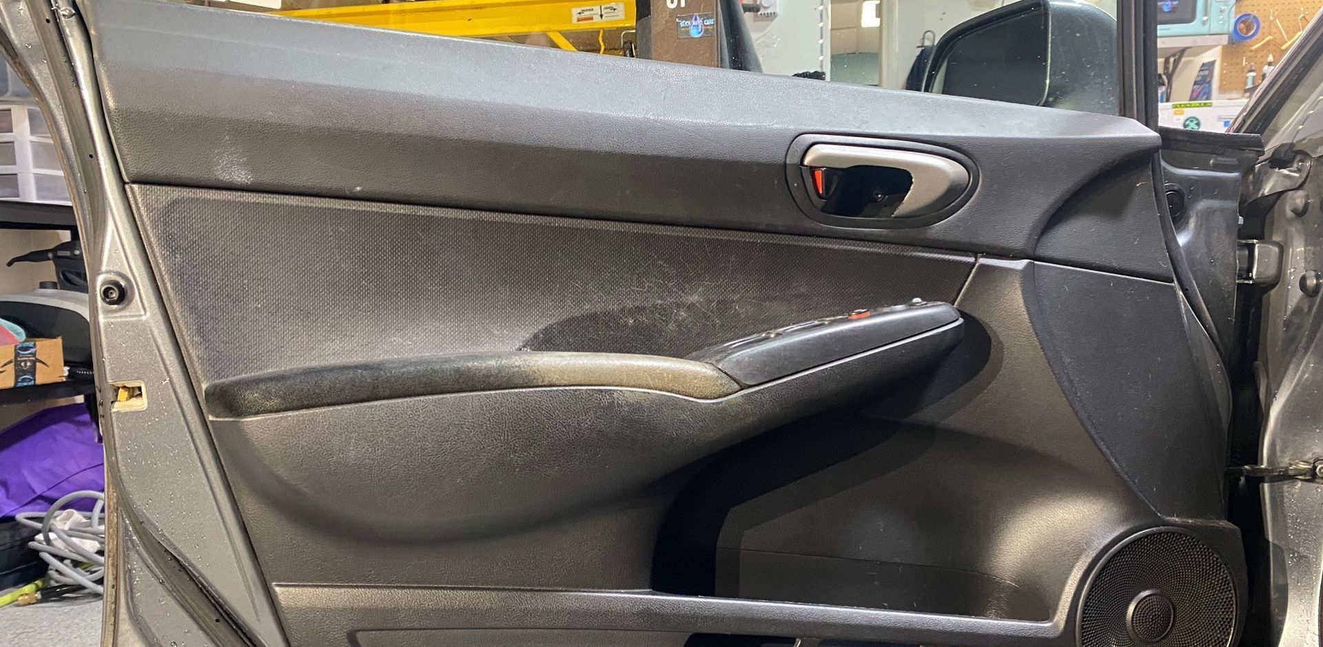 Car door interior with black and grey plastic paneling, including a door handle and armrest.