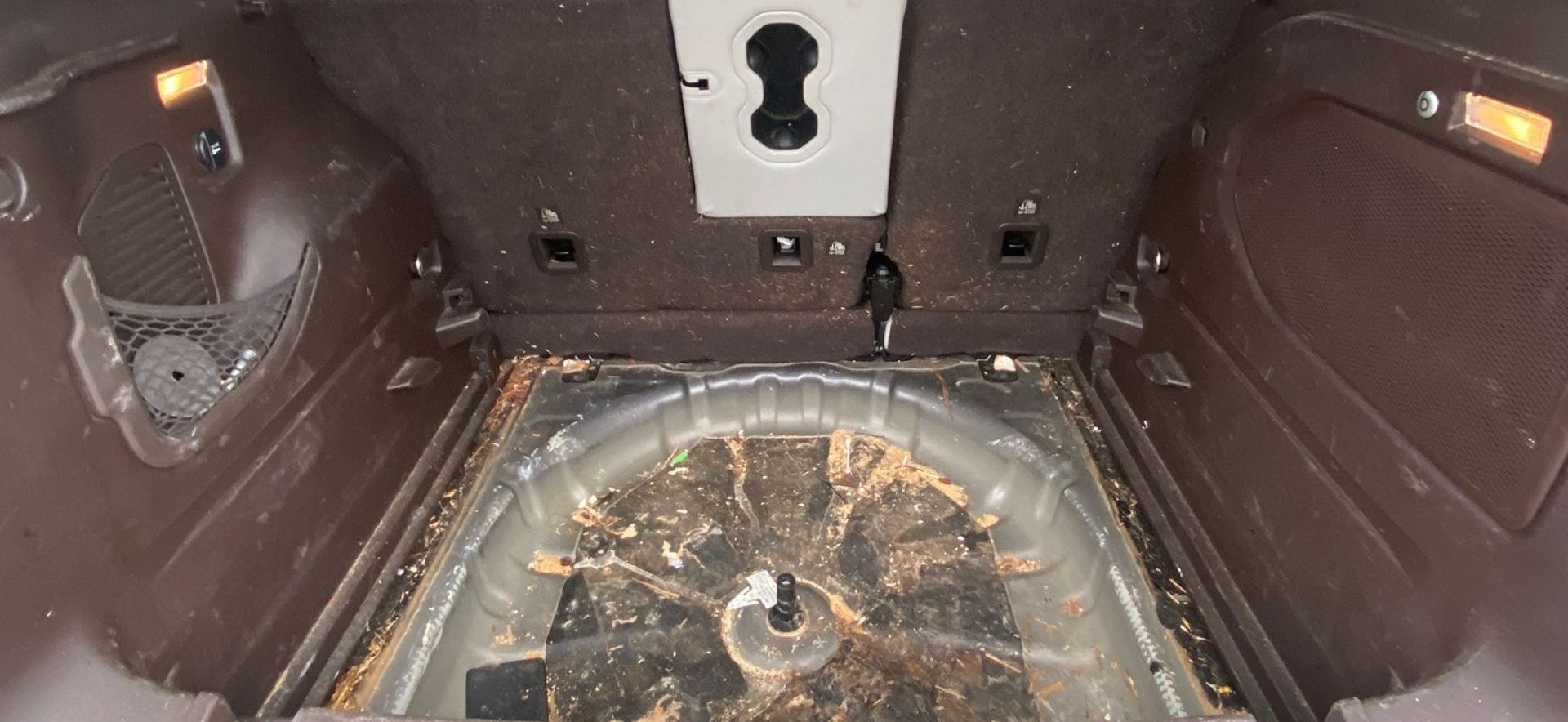 Dirty car trunk interior with exposed metal floor and various debris.