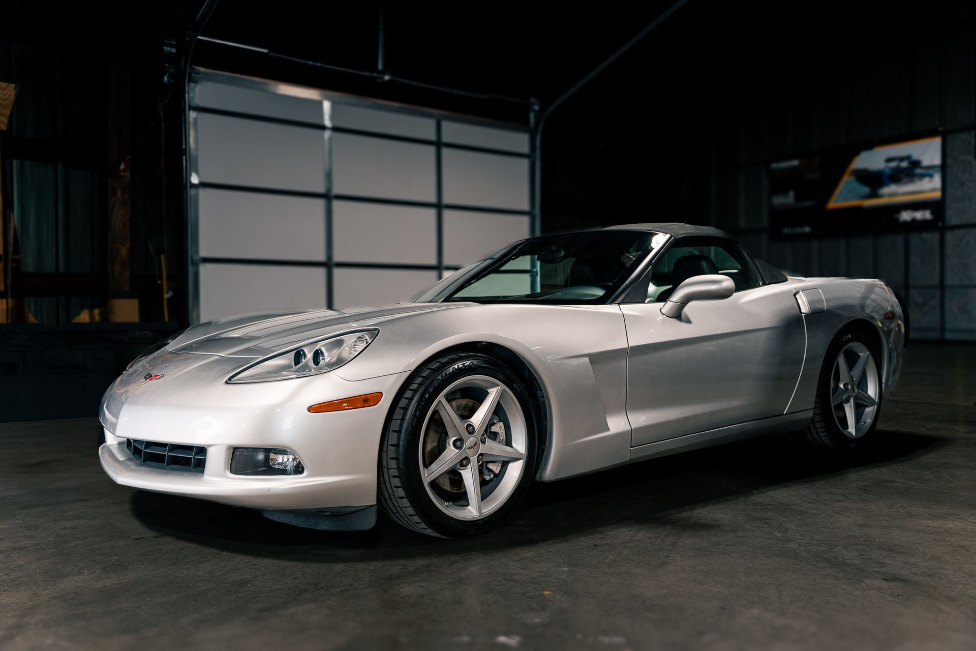 Silver convertible sports car parked in a dim garage, angled front view