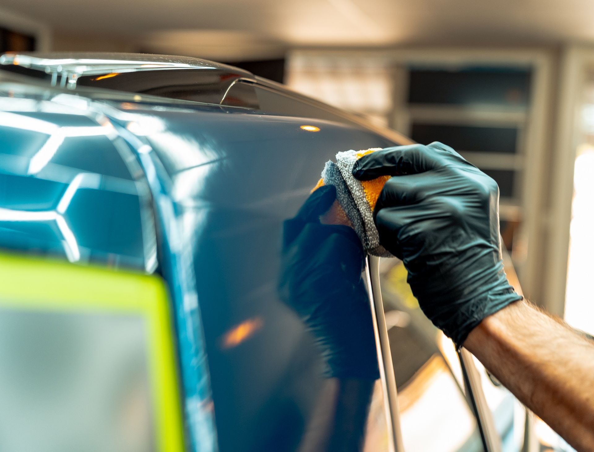 Gloved hand polishing a blue car with a cloth in a garage