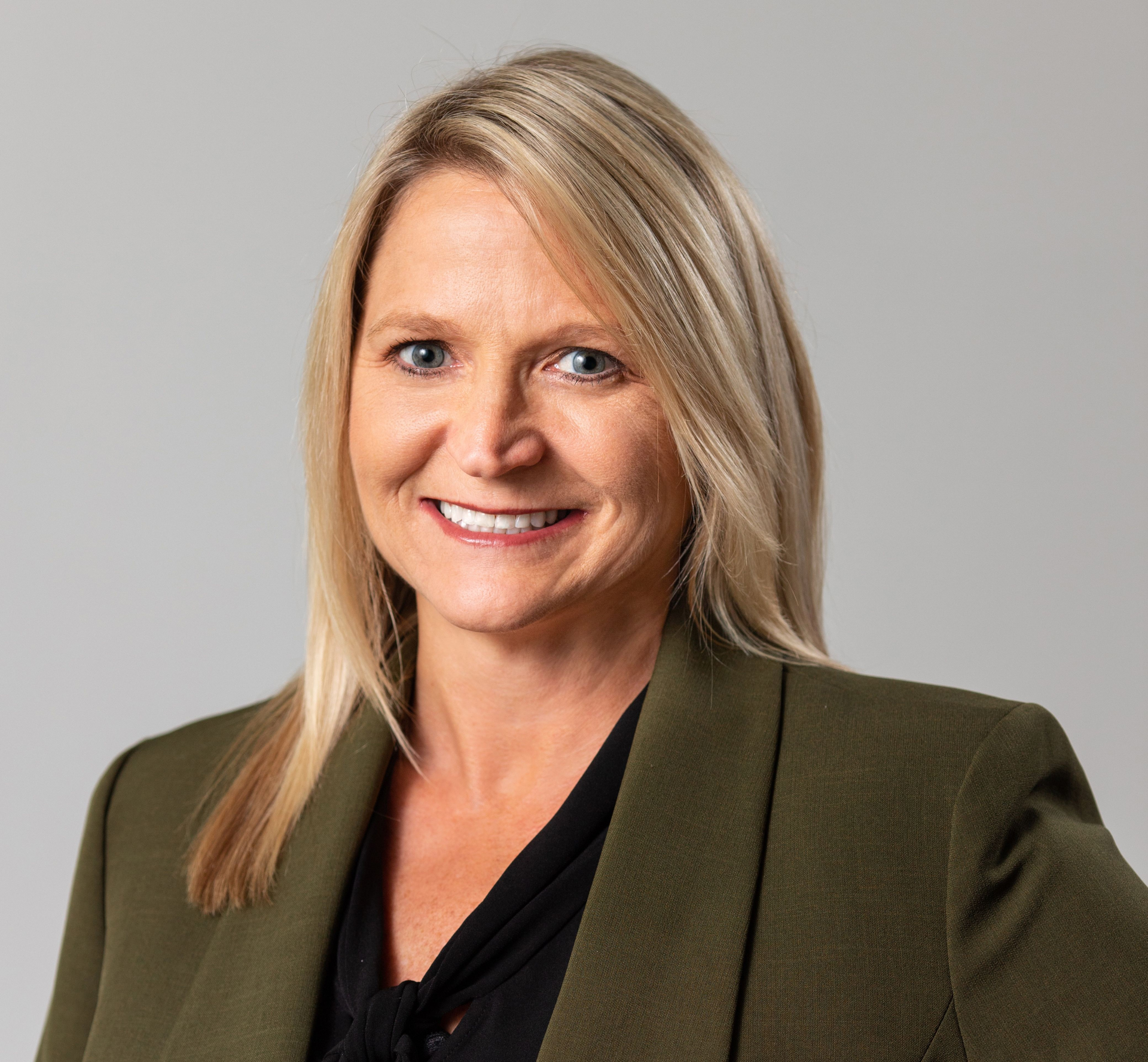 Portrait of a smiling woman in an olive blazer against a gray background