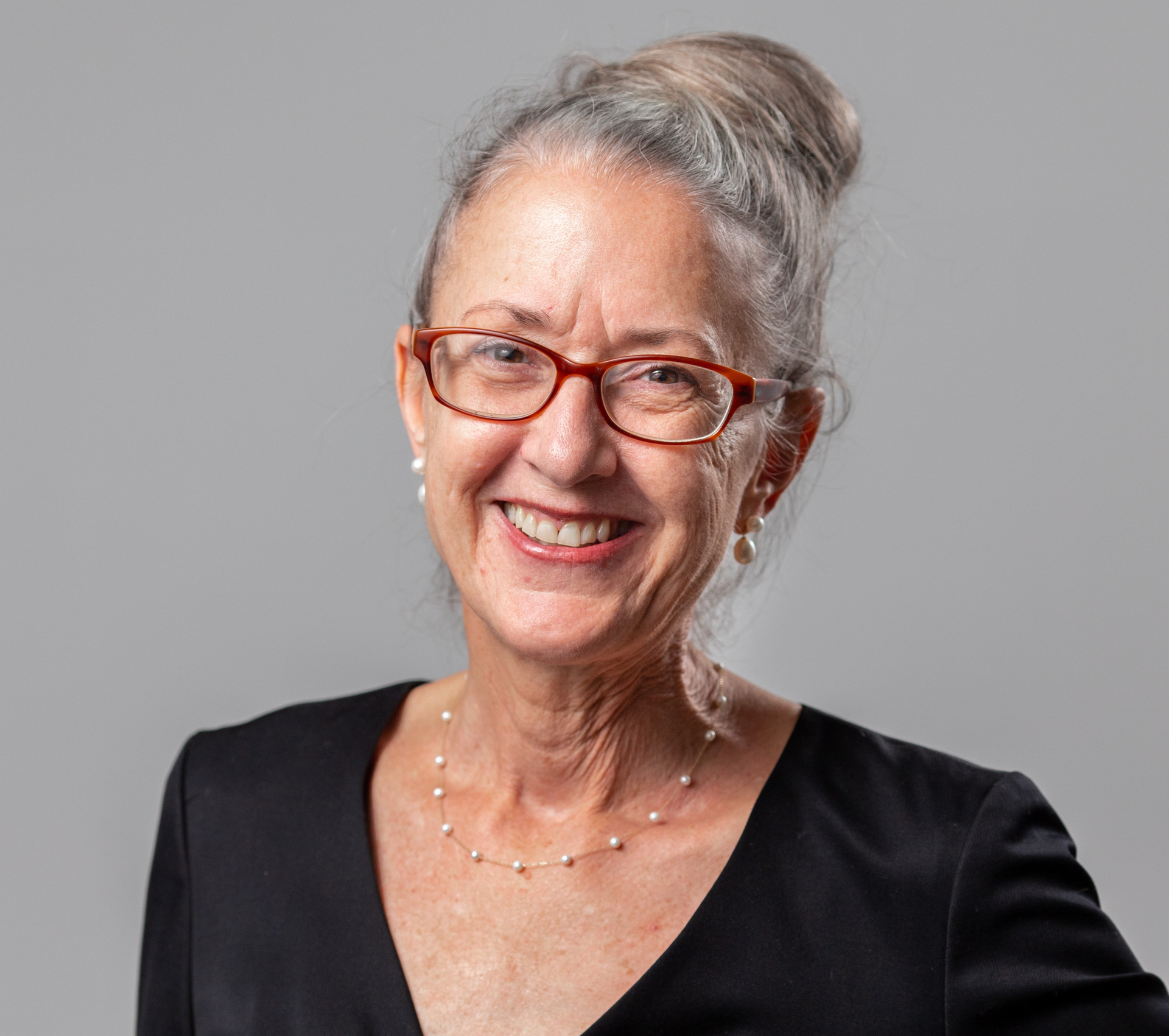 Smiling woman with gray hair and red glasses against a light gray background