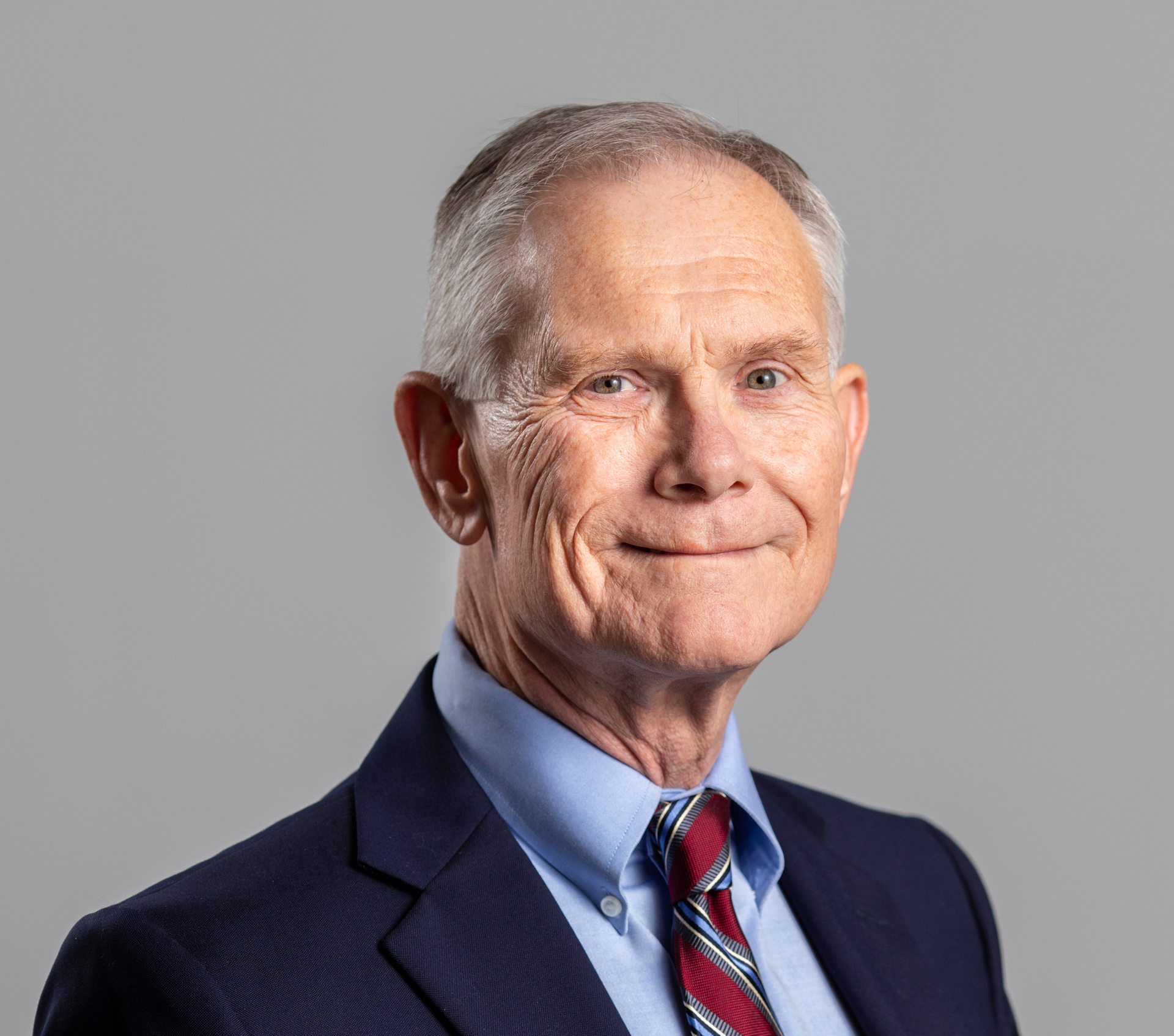 Studio headshot of a man in a navy suit and striped tie against a gray background