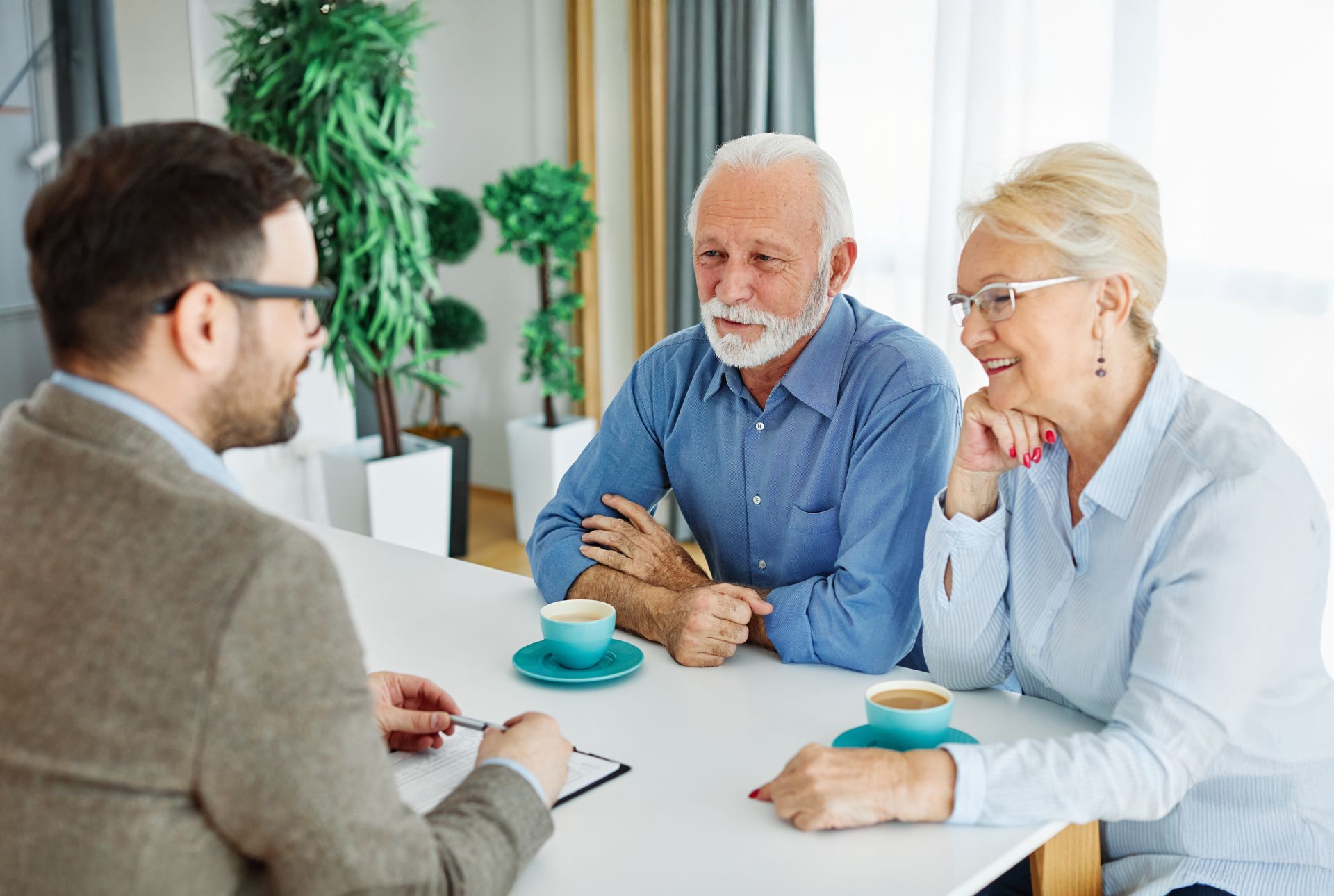 Three people in a meeting, talking around a table with coffee cups in a bright office