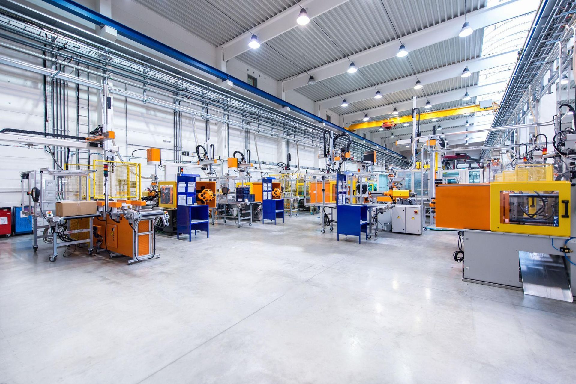 Bright industrial factory floor with orange machines, conveyors, and overhead piping in a spacious warehouse