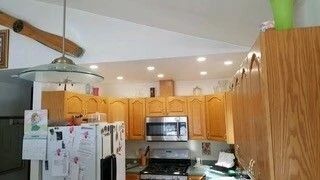 Compact kitchen with oak cabinets, white fridge, and stainless-steel stove under recessed lights.