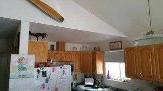 Kitchen interior with wooden cabinets, white refrigerator, window, and high vaulted ceiling with ceiling fan
