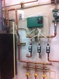 Utility room with pipes, valves, and control box mounted on a wall
