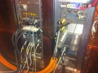 Open electrical control cabinet with wires, modules, and orange cables inside.