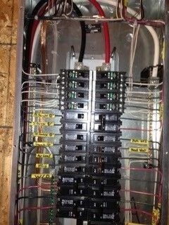 Electrical breaker panel with rows of circuit breakers and bundled red and white wires