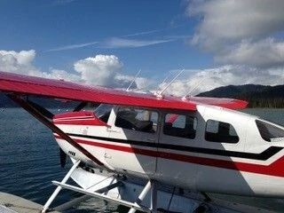Red and white seaplane floating on calm water near mountains under a blue sky