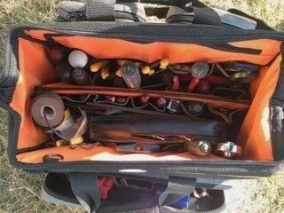 Open tool bag with orange lining filled with assorted hand tools on grass