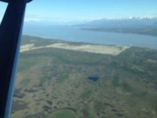 Aerial view of wetlands and water near a coastline, seen from an airplane window.