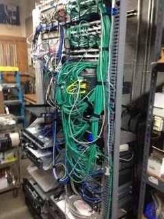 Network rack filled with tangled green and blue cables and equipment in a server room