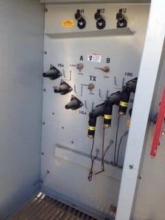 Open electrical cabinet with switches, wires, and labels inside a gray metal enclosure.