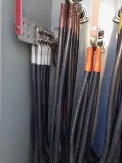 Coiled black electrical cables with orange connectors hanging on a gray wall panel.