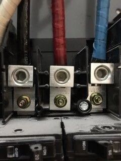 Three electrical terminal blocks with red, black, and blue cables inside a panel, above circuit breakers.