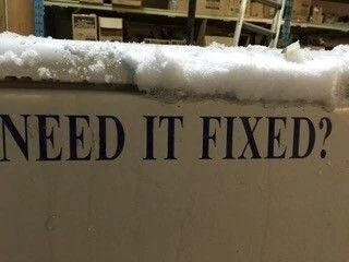 Snow-covered sign with the words “NEED IT FIXED?”